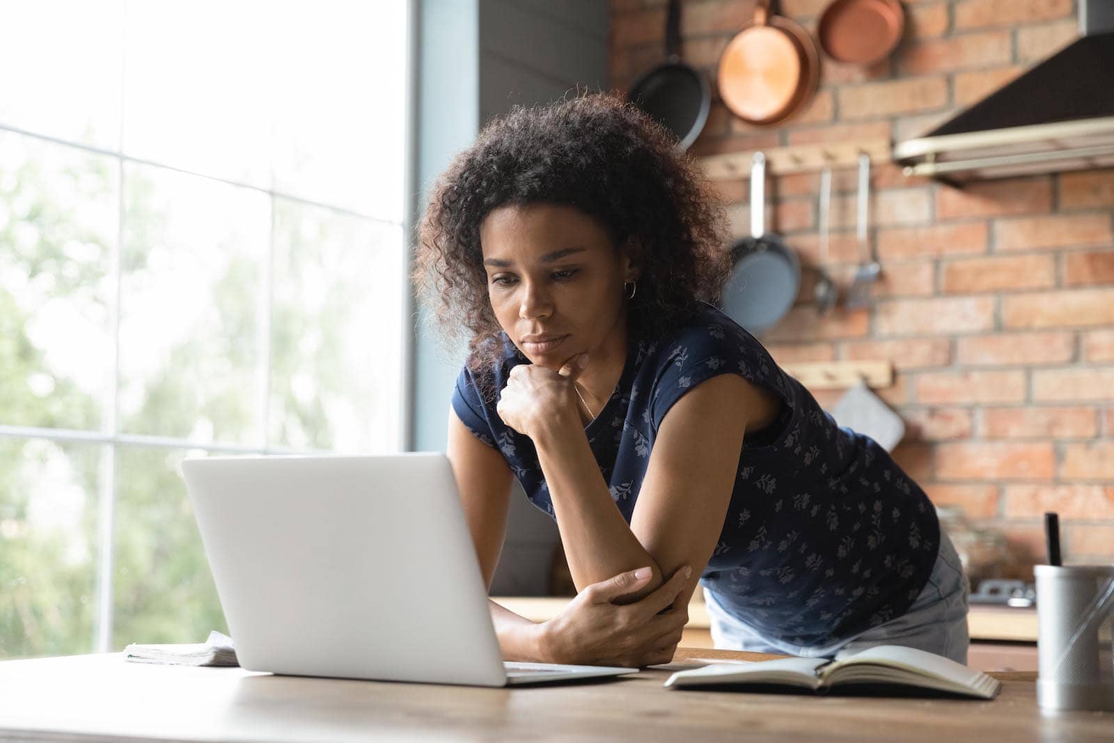 Thoughtful african american woman stand by work desk at home office look at laptop screen create new decision consider idea. Young black woman freelancer student focused on computer think on research